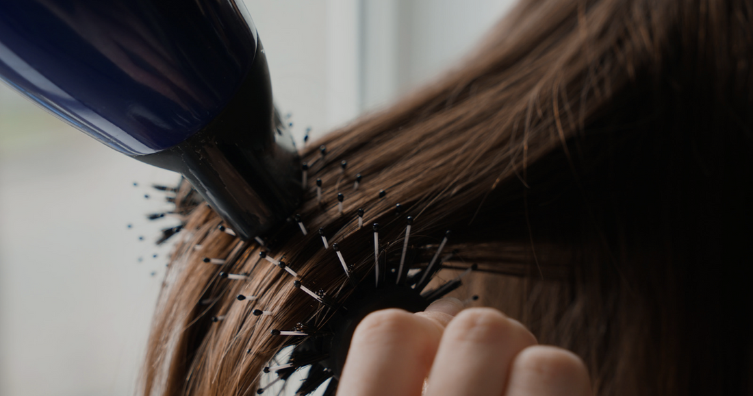 Close-up of brown hair being blow dried with a round brush and hairdryer at home