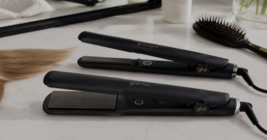 GHD IV Original Styler and GHD Max Styler side by side on a bathroom vanity, showing the difference in plate width for short, medium, long and thick hair styling.